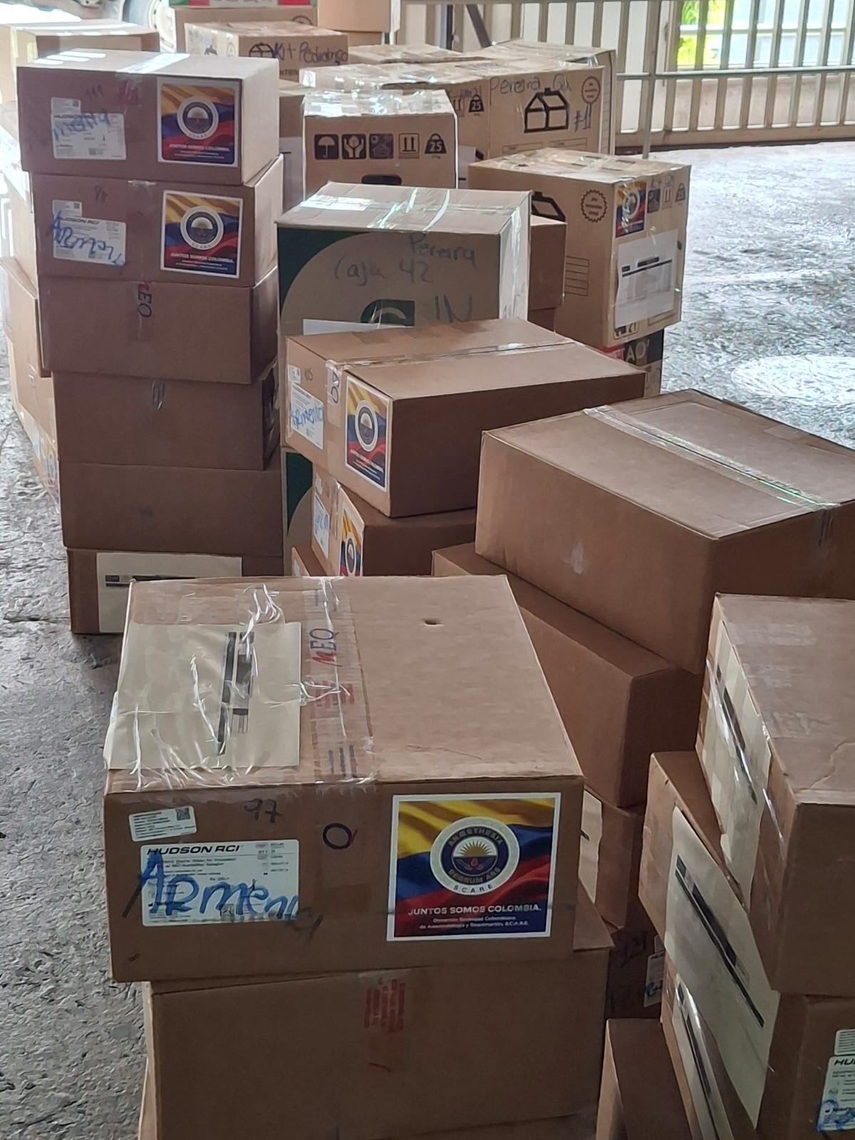 Cajas de donaciones apiladas con el sello Juntos Somos Colombia, marcadas por ciudad de destino.
