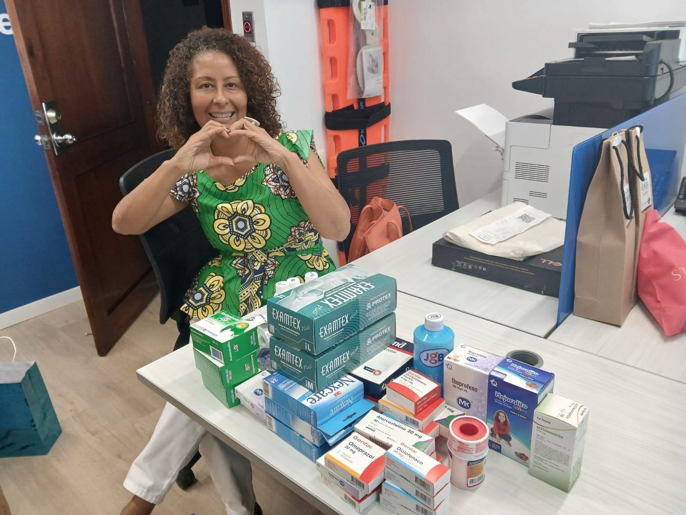 Voluntaria mostrando medicamentos e insumos médicos donados sobre un escritorio.